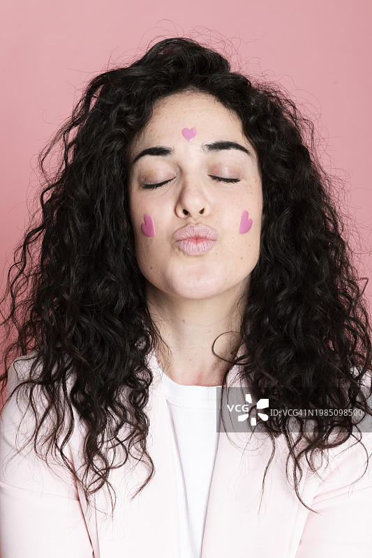 女人撅着嘴，脸上贴着心形贴纸，背景为粉色图片素材