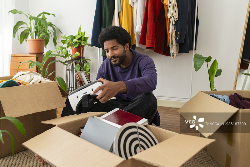 男人在整理物品，看着盒子附近的虚拟现实模拟器图片素材