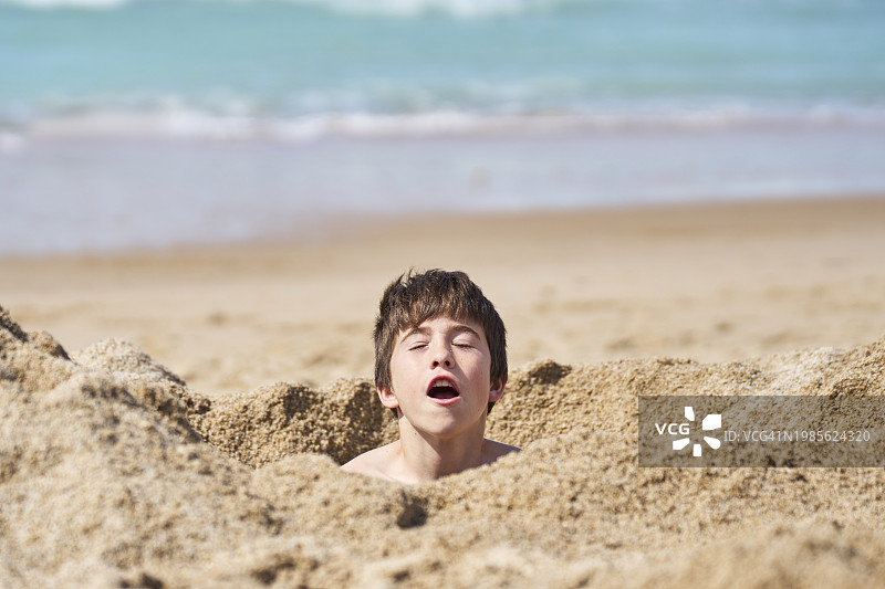 海滩上埋在沙子里的闭眼男孩肖像图片素材