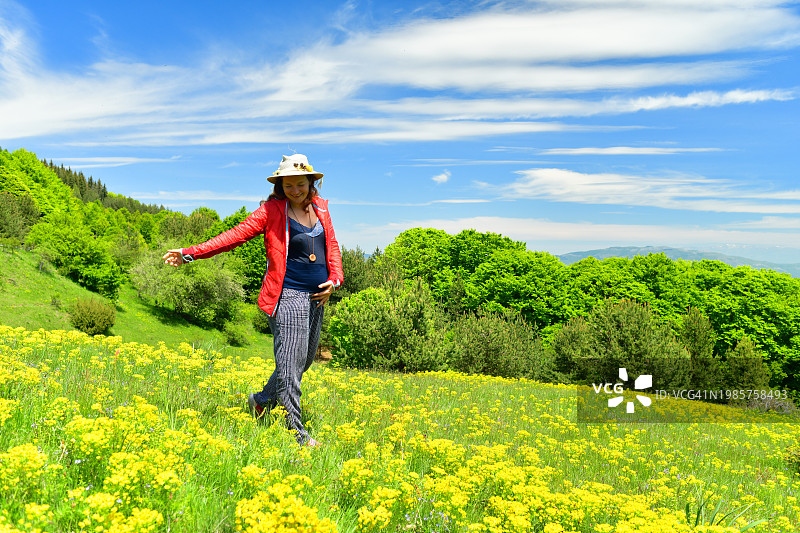 孕妇在阳光明媚的户外野花草甸中享受时光图片素材