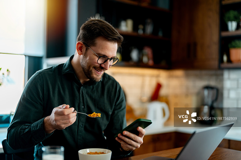 男人在厨房餐桌旁用早餐时使用智能手机图片素材