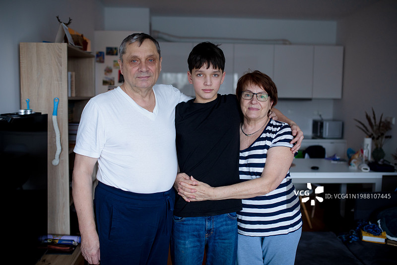 温馨的祖父母与青少年孙子在舒适的客厅里并肩站立图片素材