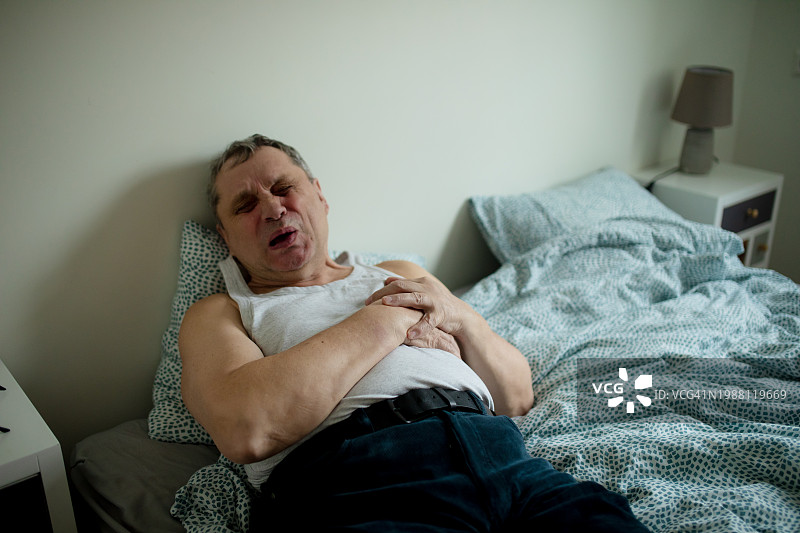 面带痛苦表情的老年男人躺在床上，手按着左胸图片素材