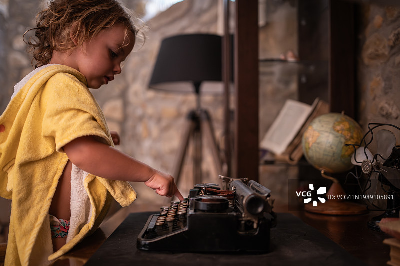 漂亮的金发小女孩在玩古董打字机。图片素材
