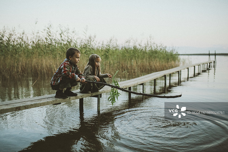 男孩和女孩蹲在湖中的木板上图片素材