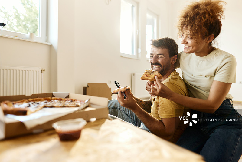 快乐的夫妇在家装休息期间使用手机吃披萨图片素材
