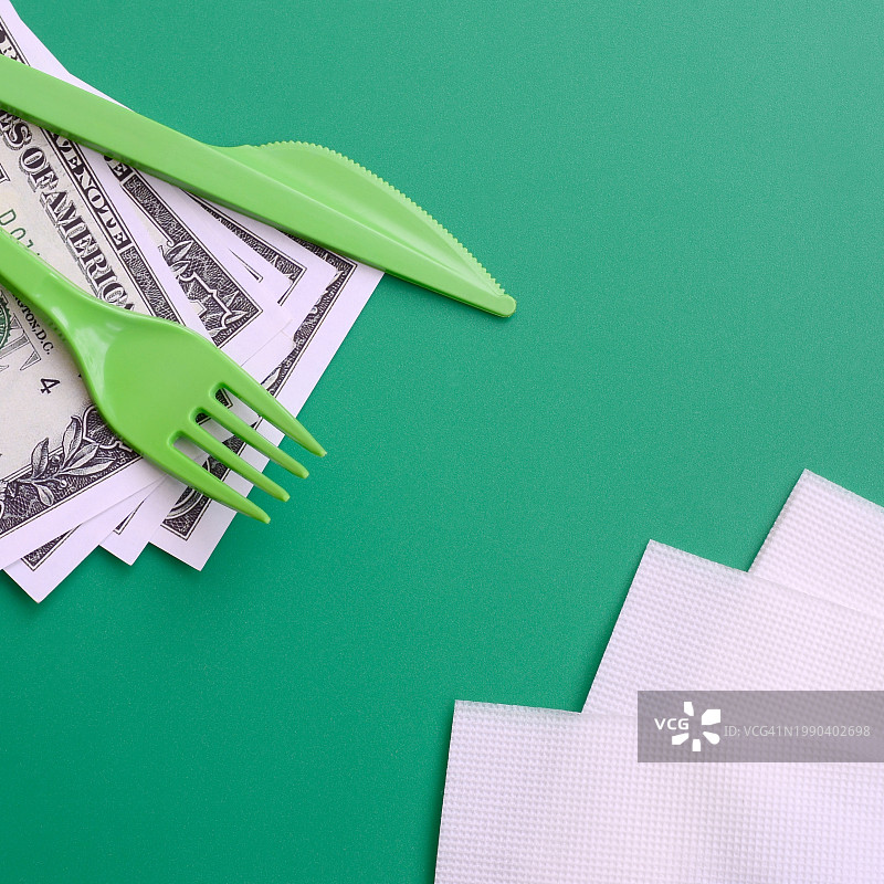 绿色背景上的塑料叉子和餐刀俯视图图片素材