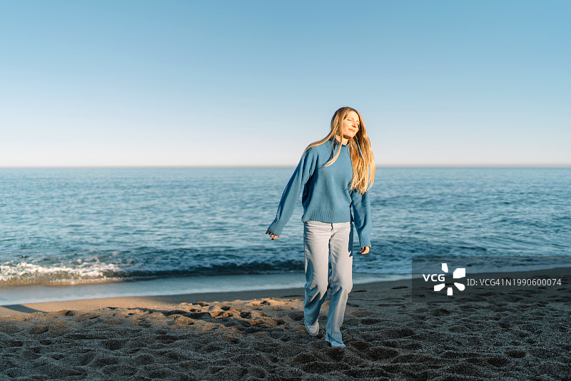 站在晴朗天空下海滩上的年轻女子肖像图片素材