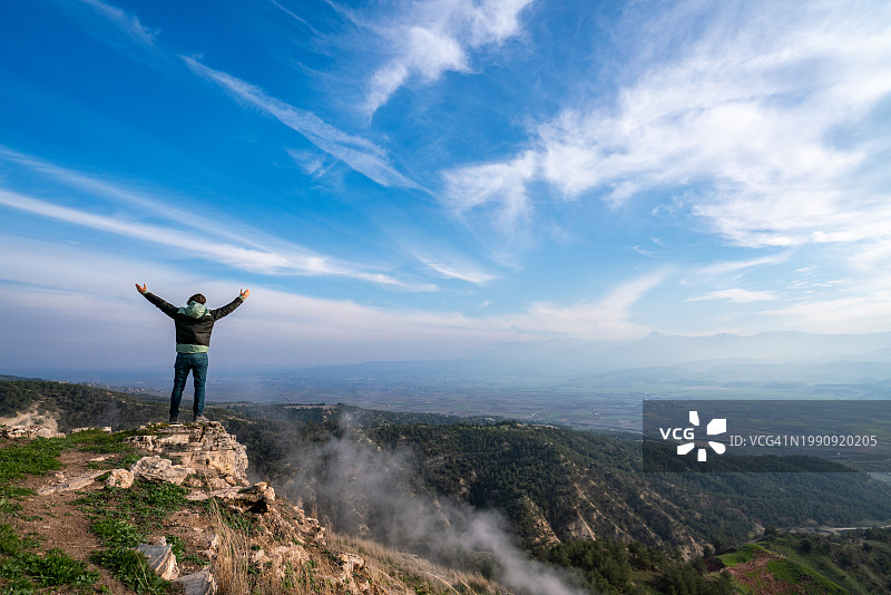 在有雾的天气里，一位成功的登山者在山顶张开双臂图片素材