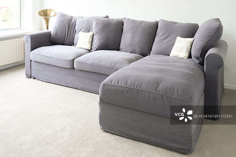 客厅里一张灰色的大型舒适沙发，配有大小靠垫，背景是留声机和透明玻璃窗图片素材