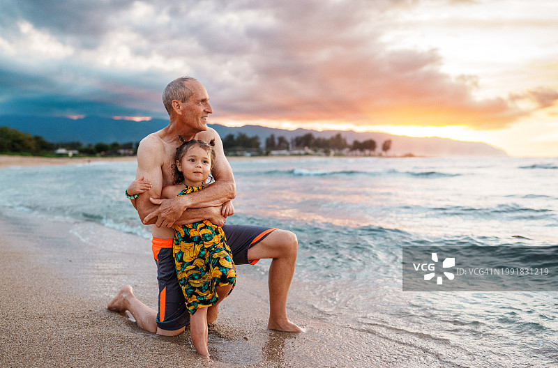 快乐的小女孩和她的爷爷在海滩欣赏日落图片素材