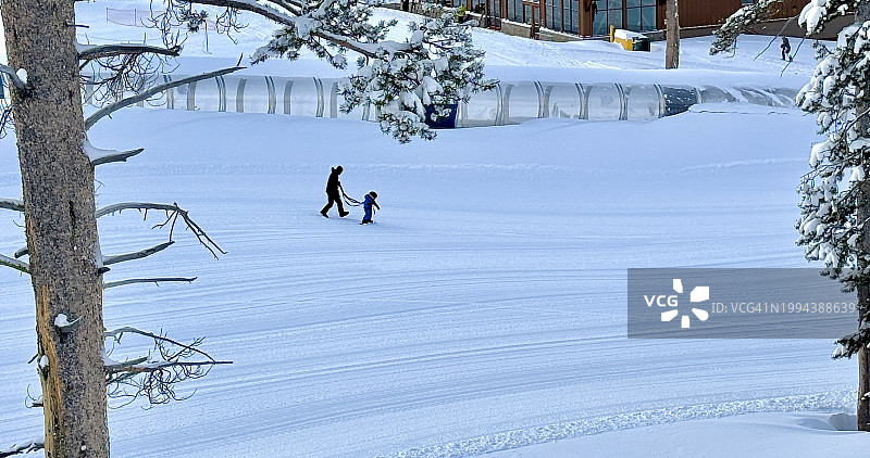成年家长在糖碗滑雪胜地学习区，在高 Sierra 山脉加州，犹大旅馆背景下，用安全绳在空的魔毯上教孩子滑雪图片素材