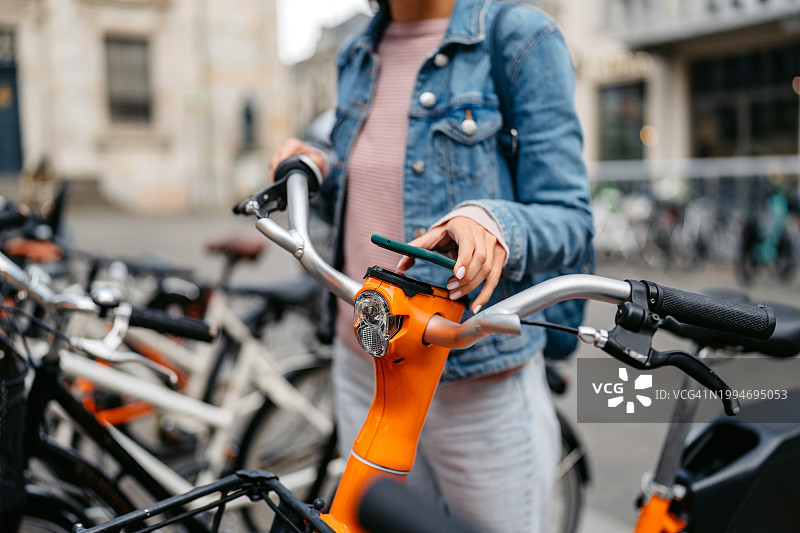 年轻女人在丹麦哥本哈根用手机租电动自行车图片素材
