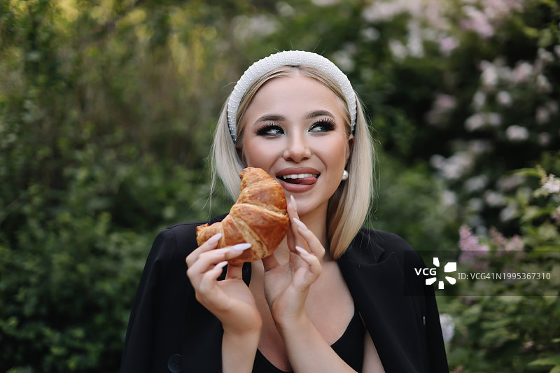 在绿色公园野餐时吃牛角面包的微笑女性肖像图片素材