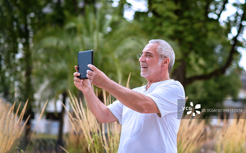 快乐的老年男人用平板电脑拍照图片素材