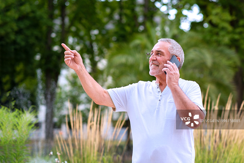 快乐的老人留着胡子，戴着眼镜，微笑的老年商人，推销员，企业家拿着他的手机图片素材