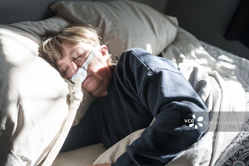 患有睡眠呼吸暂停的中年妇女戴着CPAP机在床上睡觉图片素材