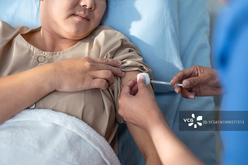 年轻护士为病人肩部接种疫苗特写。有魅力的中年妇女躺在床上，在医院病房的恢复室接受医生治疗并输液。图片素材