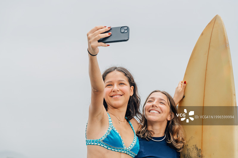 女朋友们在海边拥抱自拍，手里拿着冲浪板图片素材