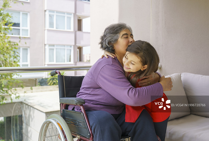 孙女在阳台上拥抱坐在轮椅上的奶奶图片素材