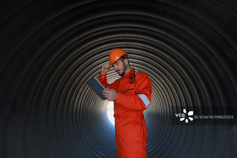 工地工程师在大型污水排水管内的隧道施工现场使用平板电脑图片素材