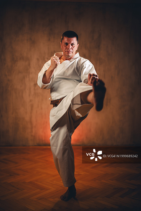 中年男子身穿白色和服，在深色背景墙前练习空手道图片素材