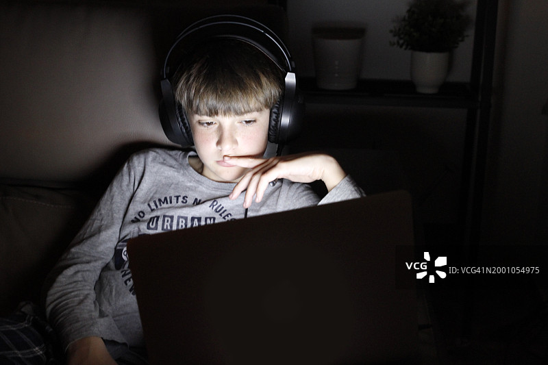 男孩晚上在沙发上使用笔记本电脑图片素材