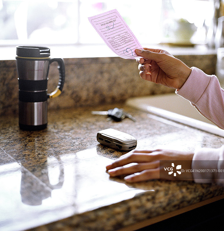 女人看着厨房台面上的便条、手机和钥匙图片素材