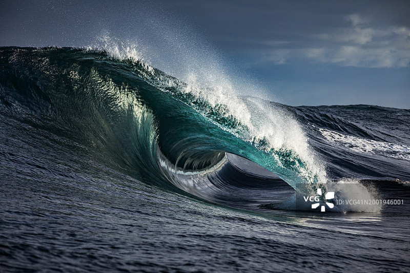 清晨阳光下礁石上涌起的蓝色巨浪图片素材