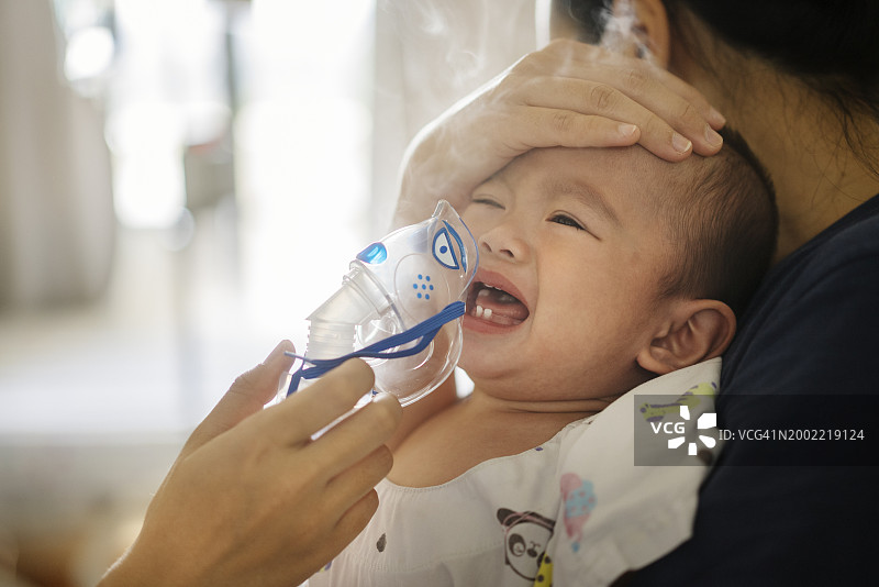 亚洲母亲用雾化器为幼儿儿子做吸入治疗图片素材