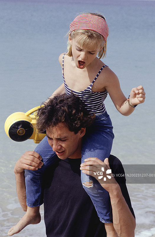 年轻男子扛着女孩（6-7岁）在海滩上行走图片素材