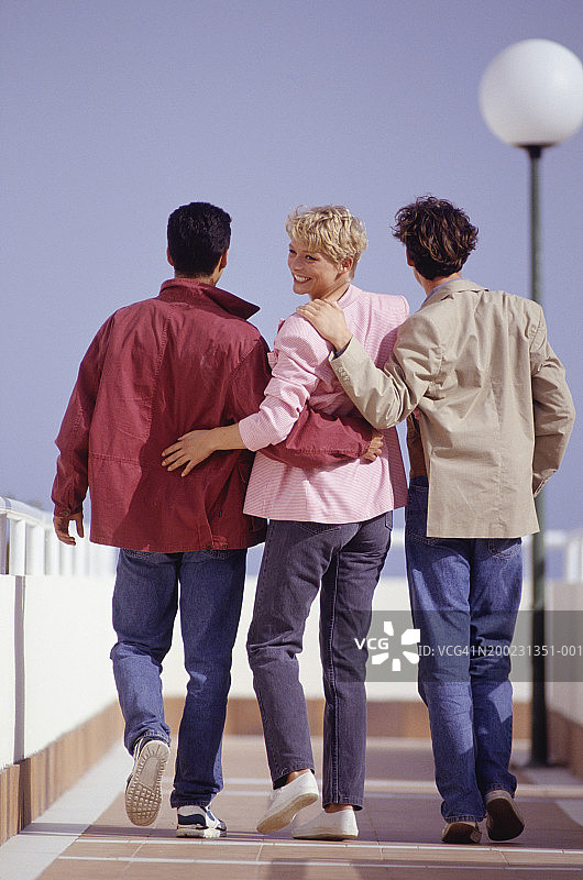 在长廊上拥抱行走的三个年轻朋友图片素材