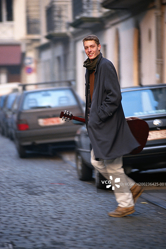 男人抱着吉他过马路图片素材