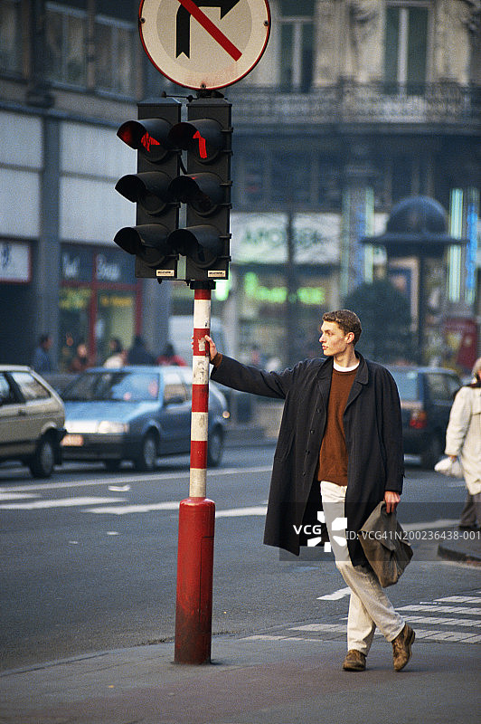 男子倚靠在路边的交通信号灯上图片素材