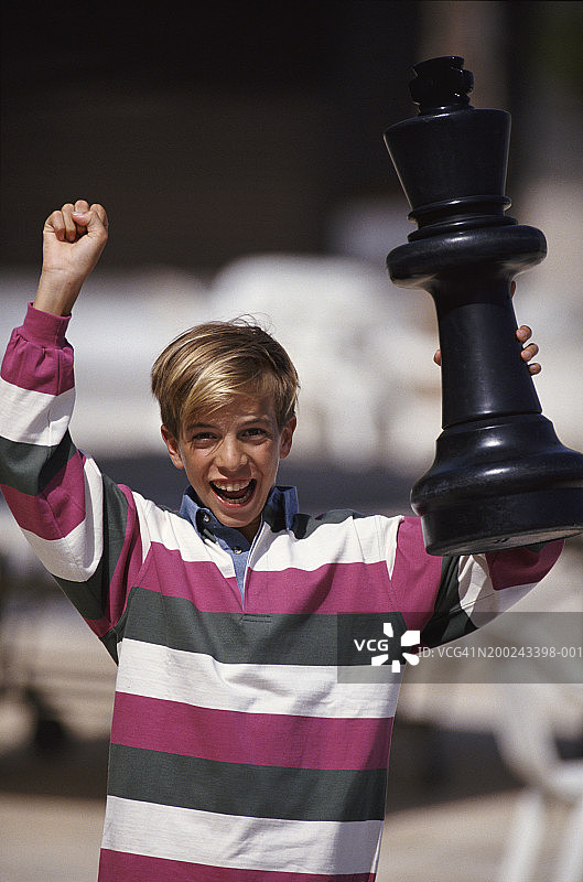穿条纹衬衫的男孩拿着巨大的棋子图片素材