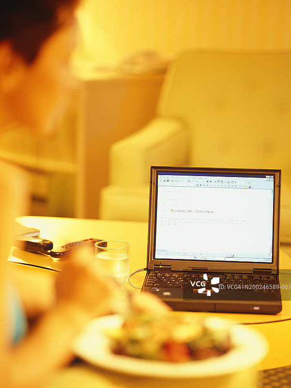 在酒店房间里一边吃东西一边使用笔记本电脑的女人图片素材