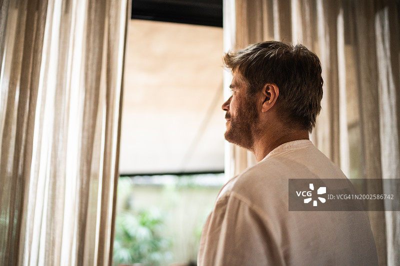 年长的男人在家中透过窗户向外看图片素材
