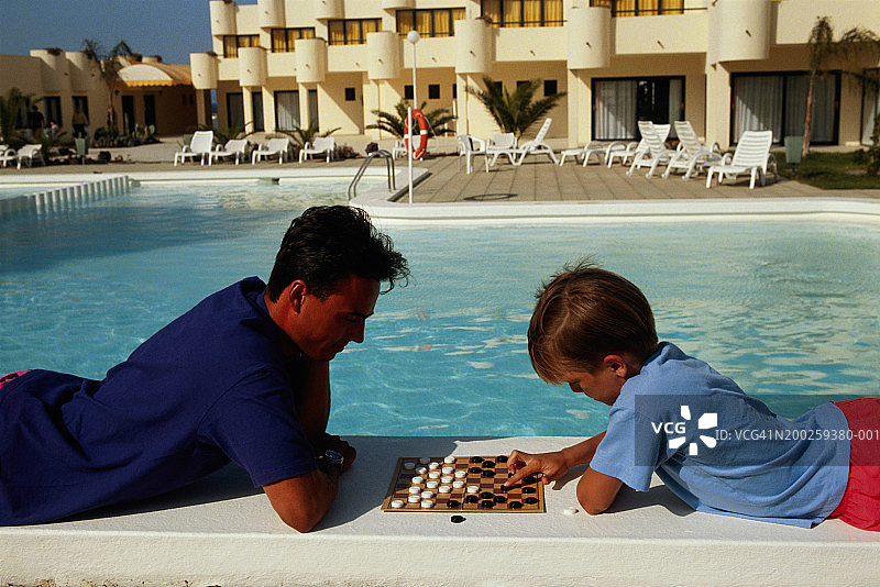男孩在泳池边移动棋盘上的棋子图片素材