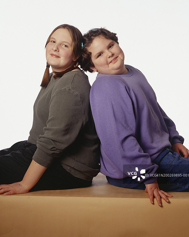 姐妹(10-11岁)(12-13岁)背靠背在工作室摆姿势，肖像图片素材