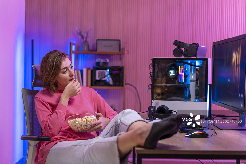 坐在电脑前吃爆米花的微笑年轻金发女子图片素材