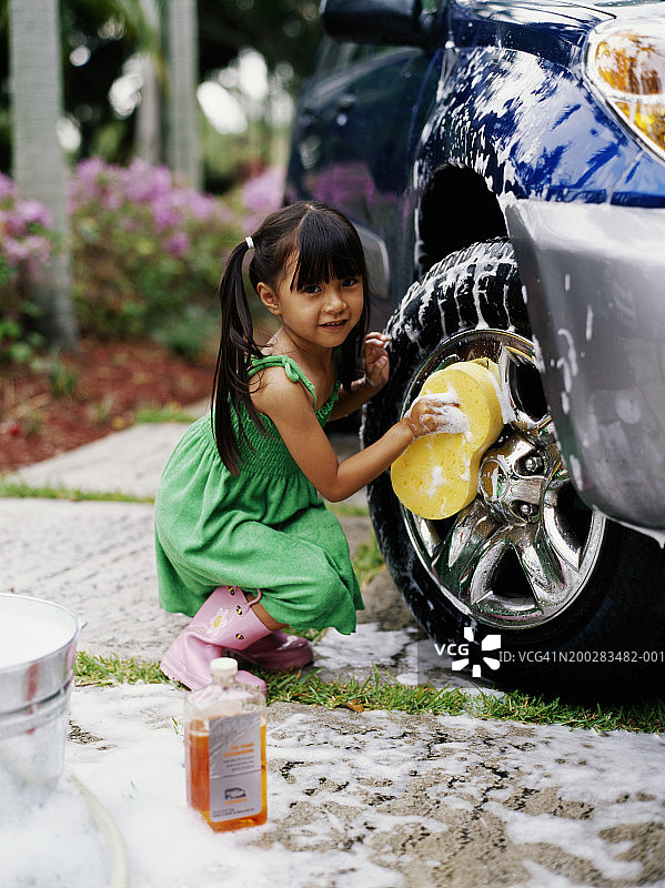 女孩（4-6岁）用海绵清洗汽车车轮，微笑，肖像图片素材