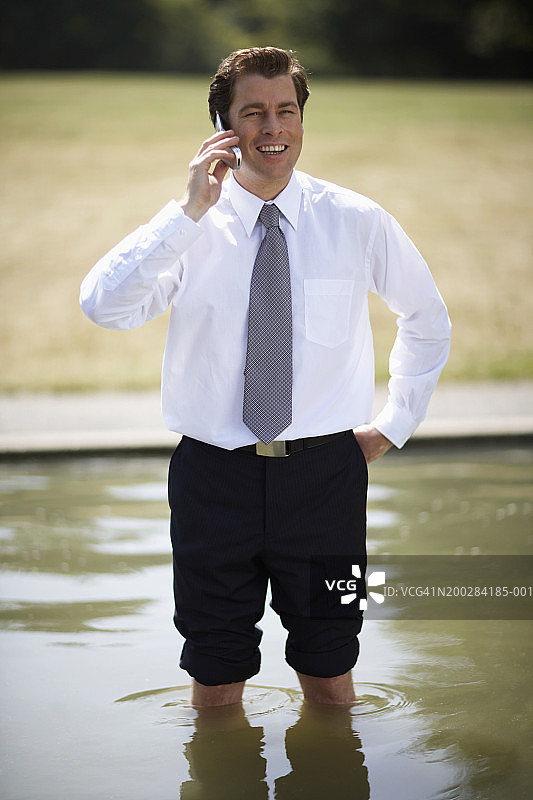 商人站在池塘边使用手机微笑图片素材