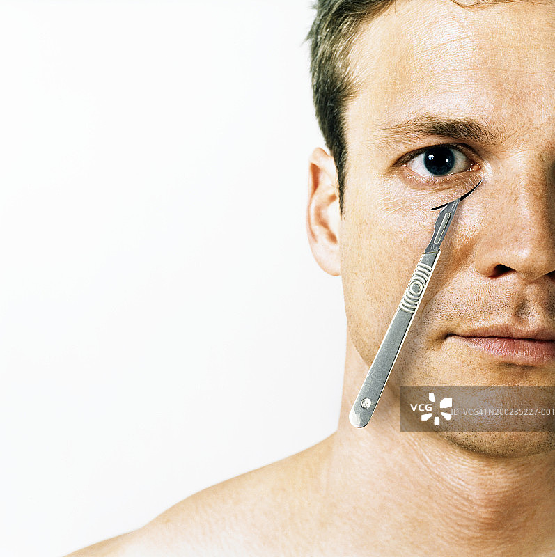 用手术刀“切割”眼下的男人，肖像图片素材