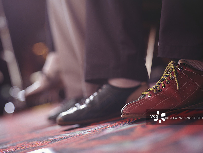 穿着保龄球鞋坐在保龄球馆里的男人，低角度图片素材