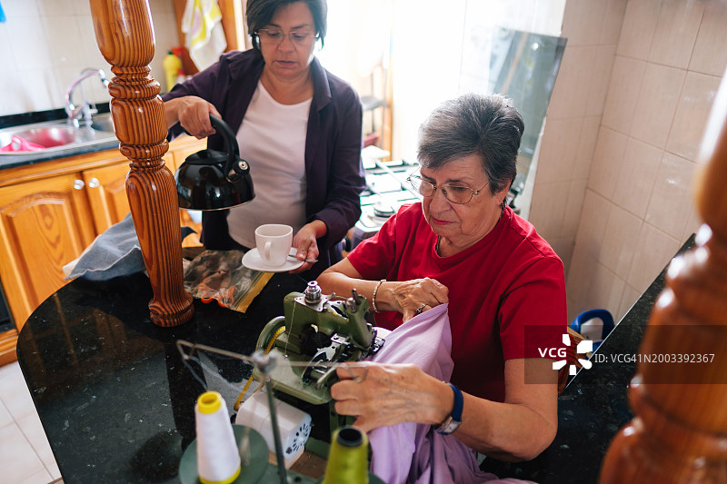 女儿奉茶时在家缝纫的年长女性图片素材