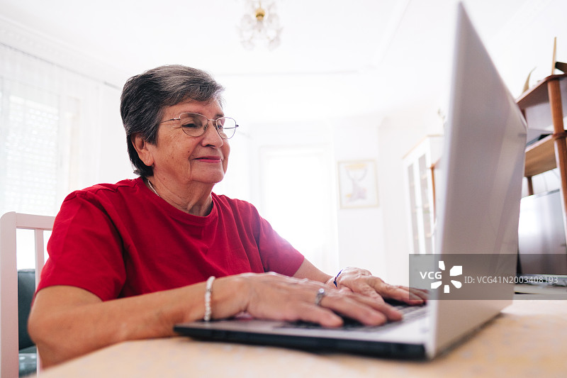 在家中使用笔记本电脑并面带微笑的年长妇女图片素材