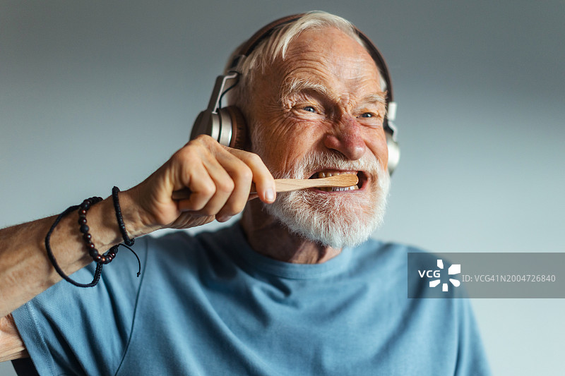 在浴室里用无线耳机听音乐刷牙的年长男人图片素材