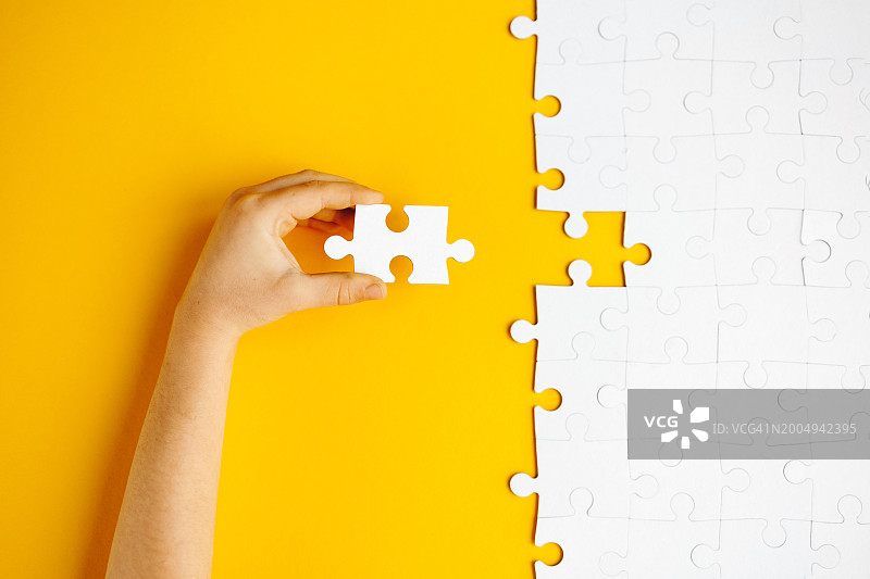 儿童将最后一块拼图放在黄色背景上图片素材