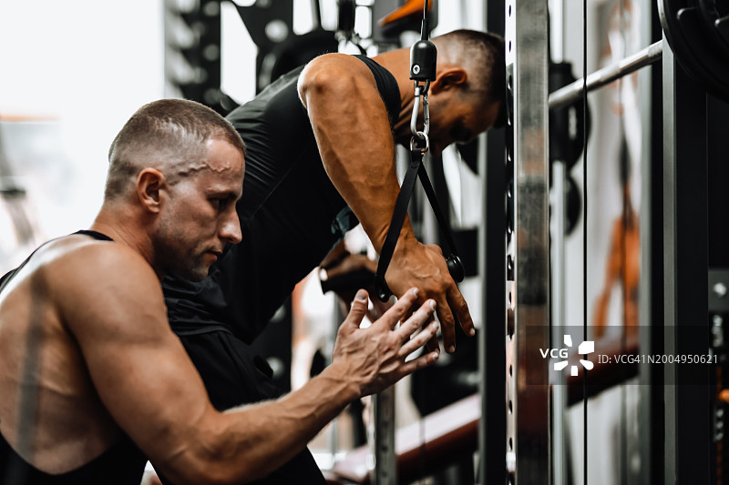 男子健身教练帮助运动员进行拉力器械训练图片素材