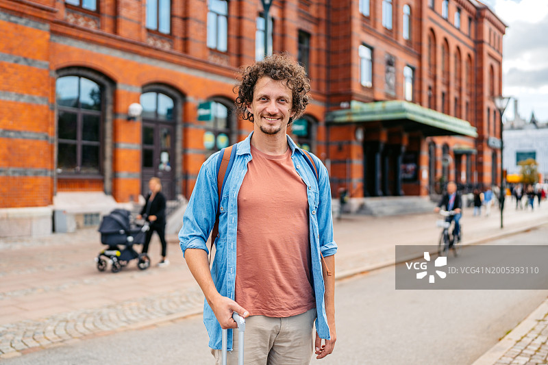 一个带着行李的成年男子站在马尔默火车站前图片素材